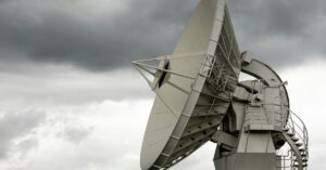 A large satellite dish points towards a cloudy, overcast sky, conveying a sense of technology and communication amidst a stormy atmosphere.
