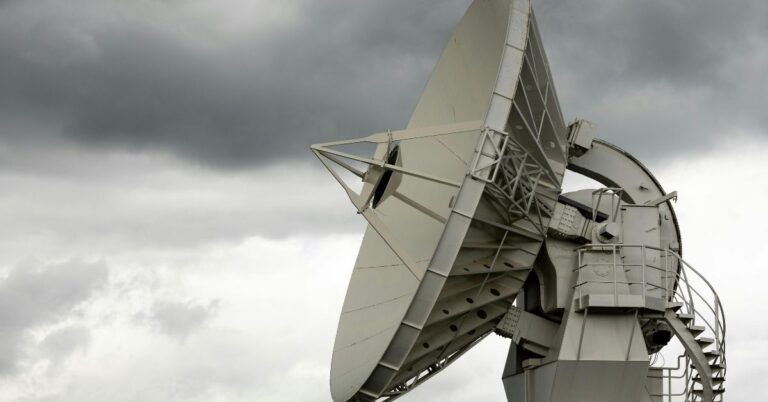 A large satellite dish points towards a cloudy, overcast sky, conveying a sense of technology and communication amidst a stormy atmosphere.