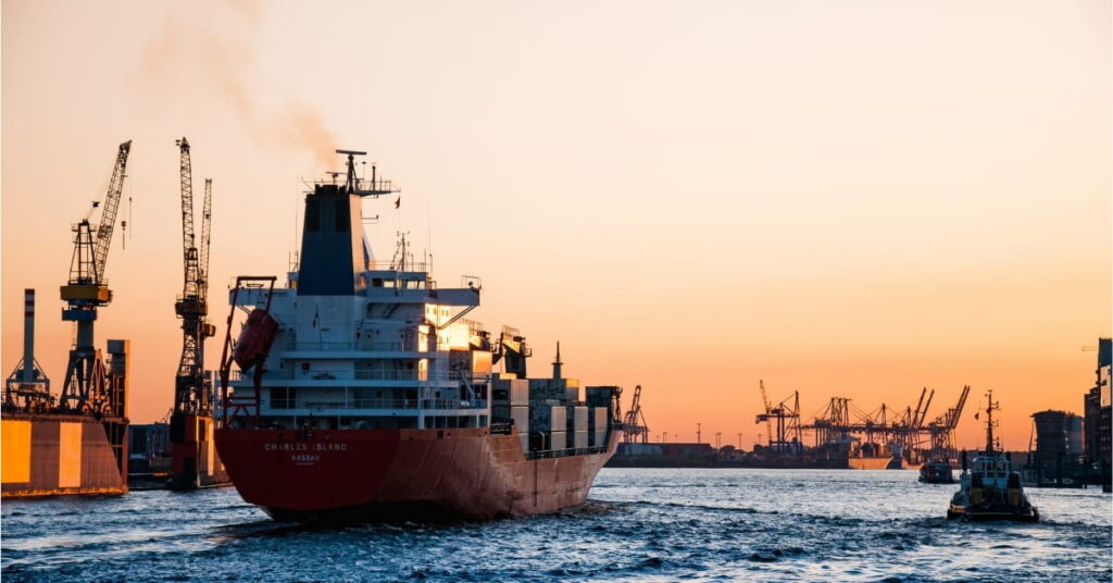 A large cargo ship sails on the water during a vibrant sunset